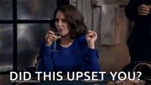 a woman is sitting at a table drinking a glass of wine and making a funny face .