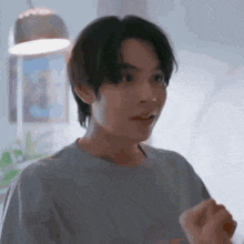 a young man in a gray shirt is standing in a room and making a funny face .
