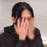 a woman is covering her face with her hands while sitting down .