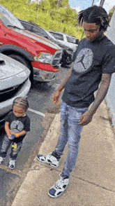 a man and a child are standing next to each other on a sidewalk next to a parking lot .