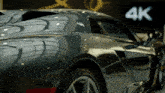 a black sports car is parked in front of a sign that says 4k