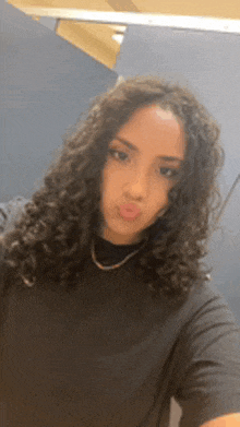 a young woman with curly hair is taking a selfie in a bathroom stall .