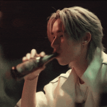 a man in a white shirt is drinking from a brown bottle