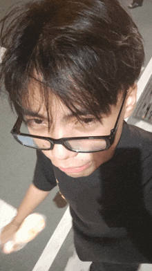 a young man wearing glasses and a black shirt looks down at the camera