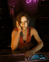 a woman in a red tank top sits at a desk with her hands folded in front of a keyboard
