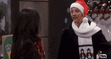 a woman wearing a santa hat and a scarf with the letters tbs on the bottom