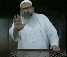 a man with a beard and glasses is standing in front of a microphone and waving his hand .