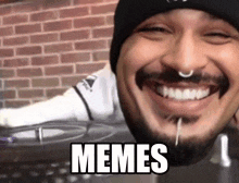 a man with a beard and a nose ring is smiling with the word memes on his face .