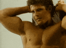 a shirtless man with a towel around his neck looks at the camera