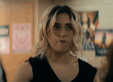 a woman with blonde hair is wearing a black tank top and making a face .