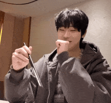a young man in a gray jacket is holding a pen in his hand