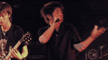 a man singing into a microphone while another man holds a guitar