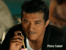 a close up of a man eating with a straw and the word pisau ukur on the bottom