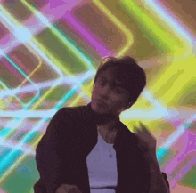 a man in a black jacket is dancing in front of a colorful background .
