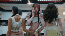 a group of women are standing in a kitchen and one of them is wearing a crop top with polka dots on it
