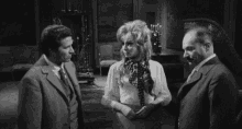 a black and white photo of a woman screaming while standing next to two men in a room .