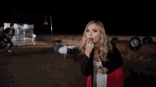 a woman is applying red lipstick in front of a car that has rolled over