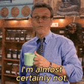 a man in a blue shirt and tie is holding a green mug and says " i 'm almost certainly not "