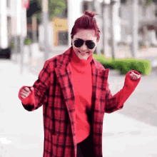 a woman wearing sunglasses and a red plaid coat is dancing