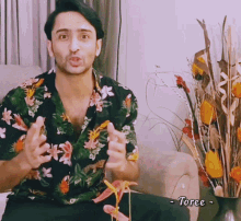 a man in a floral shirt is sitting in front of a vase of flowers with the name toree written below him