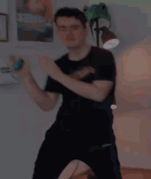 a man in a black shirt is dancing in a room with a lamp and a frog hat .