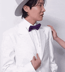 a man in a white suit with a purple bow tie and hat