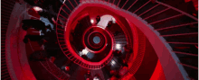 a group of people are walking down a spiral staircase in a dark room with red lights .