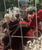 a woman in a red dress with a crown on her head is behind a fence