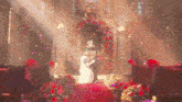 a bride and groom are kissing at their wedding in a church surrounded by flowers and confetti .