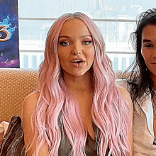 a woman with long pink hair is sitting on a couch with another woman .