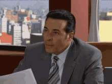 a man in a suit and tie is sitting in front of a window holding a piece of paper