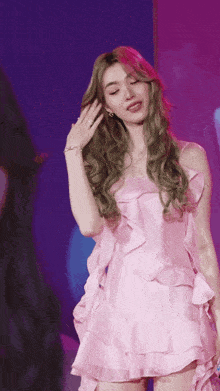 a woman in a pink dress is standing in front of a purple backdrop