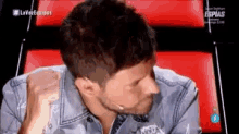 a man in a denim jacket is sitting in front of a red chair with his fist in the air .