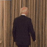 a man in a suit is standing in front of a window with curtains behind him .