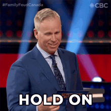a man in a suit and tie is holding a piece of paper and says hold on