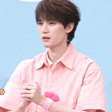 a young man in a pink shirt has a pink wristband on