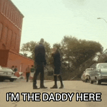 a man and a woman are standing on a street with the words `` i 'm the daddy here '' .