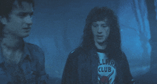 a man wearing a hellfire club t-shirt stands next to another man