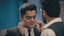 a man in a suit adjusts his earring while another man looks on