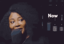 a woman is singing into a microphone and the word now is on the bottom right