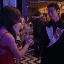 a woman in a red dress stands next to a man in a tuxedo at a party