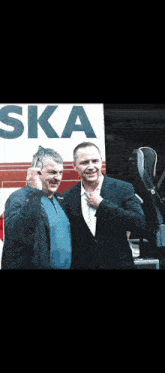 two men are posing for a picture in front of a ska sign
