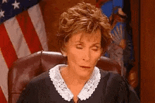 a female judge is sitting in a chair with her eyes closed in front of an american flag .