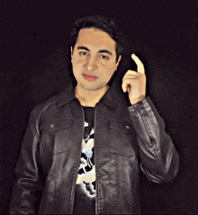 a young man wearing a black leather jacket holds up his finger