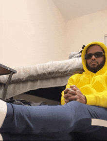 a man wearing a yellow hoodie and sunglasses is sitting on the floor