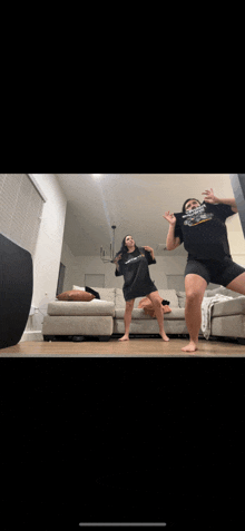 two women are dancing in a living room with one wearing a t-shirt that says ' nc state ' on it