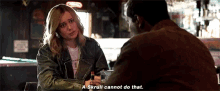 a woman in a leather jacket is sitting at a table talking to a man .