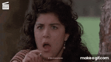 a woman with curly hair is making a funny face while standing next to a tree .