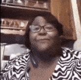 a woman wearing glasses and a zebra print shirt is smiling in a kitchen .