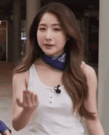 a woman wearing a white tank top and a blue bandana around her neck is giving the middle finger .